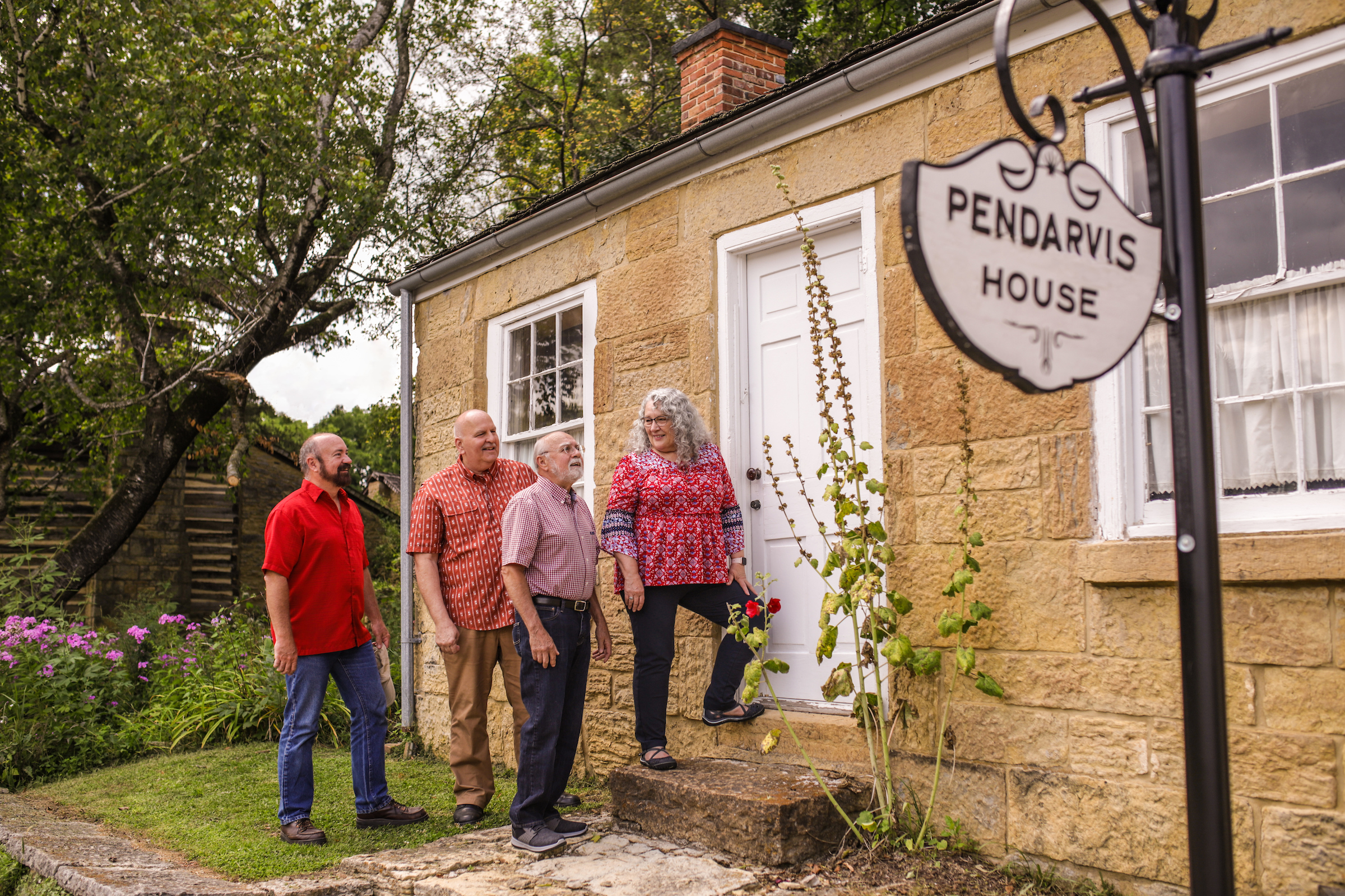 Four people in front of an old-fashioned house with a sign that says "PENDARVIS HOUSE"